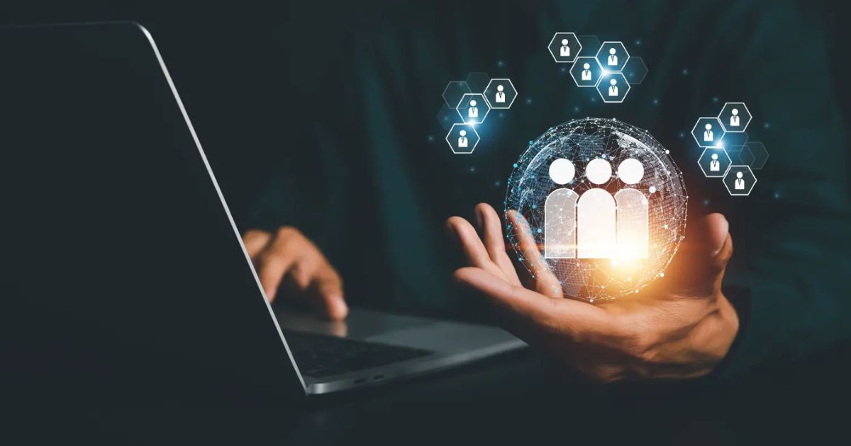 Imagem de uma pessoa utilizando um notebook, com uma mão segurando uma esfera digital brilhante contendo ícones de pessoas. Ao redor da esfera, há pequenos ícones de cadeados e perfis, representando conceitos de gestão de pessoas, recursos humanos e segurança de dados. (rh, recursos humanos, gestão de pessoas, rhtechs)