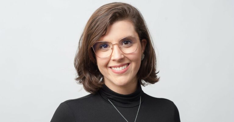 Camila Zoé Frias, executiva do Google, sorrindo para a câmera com um fundo neutro. Ela usa óculos de armação delicada e veste uma blusa preta elegante, complementada por um colar discreto, transmitindo uma imagem profissional e amigável, energia nuclear