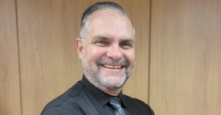 Fábio Correa Xavier, diretor do Departamento de TI do Tribunal de Contas do Estado de São Paulo (TCE-SP), sorrindo para a câmera. Ele veste uma camisa preta com uma gravata cinza, em frente a um fundo de madeira clara que confere um ambiente formal e profissional