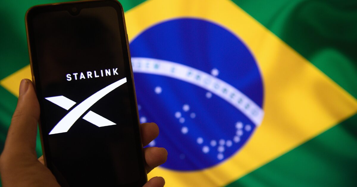 Logo da Starlink exibida em um smartphone à frente da bandeira do Brasil, simbolizando a atuação da empresa no país