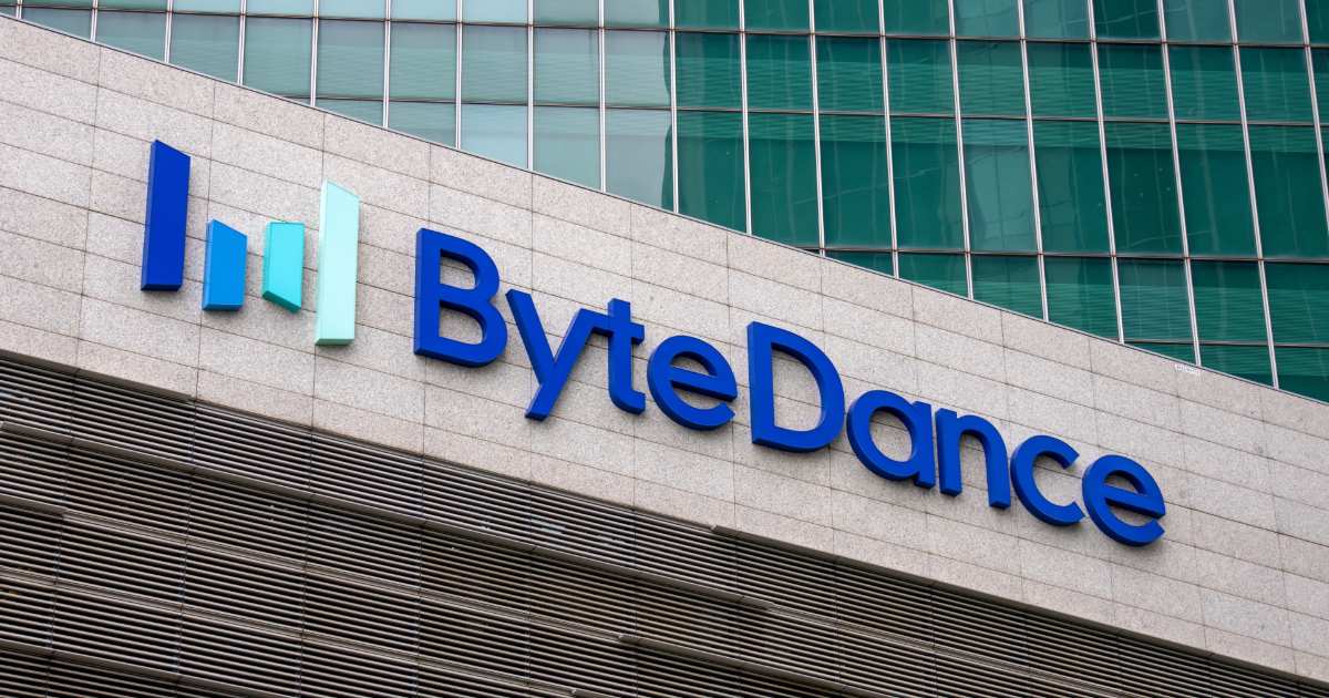 A imagem mostra a fachada de um prédio com o logotipo da ByteDance, empresa de tecnologia conhecida por ser a criadora do TikTok. O logotipo é composto pela palavra "ByteDance" em letras azuis, com um gráfico de barras coloridas (verde e azul) ao lado esquerdo, representando um crescimento ou progresso. O fundo da imagem mostra uma parede de vidro reflexiva, dando um toque moderno e corporativo ao ambiente