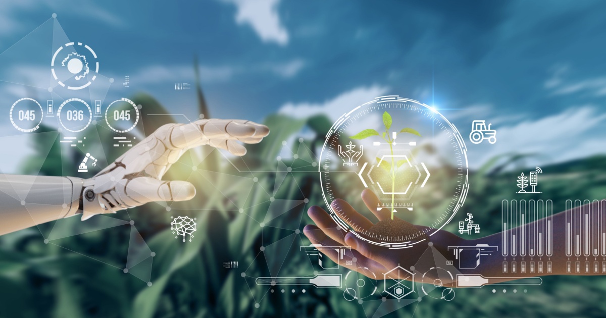 Imagem conceitual de gêmeos digitais na agricultura, mostrando uma mão robótica e uma mão humana próximas, com gráficos digitais sobrepostos. Entre elas, há um holograma de uma planta, simbolizando o uso de inteligência artificial e robótica para monitorar e replicar condições agrícolas. O fundo exibe um campo desfocado, e ícones de tecnologia e dados representam a interconexão entre o mundo físico e o digital na agricultura inteligente (gemeos digitais, digital twins, agricultura, robô, ia, inteligência artificial)