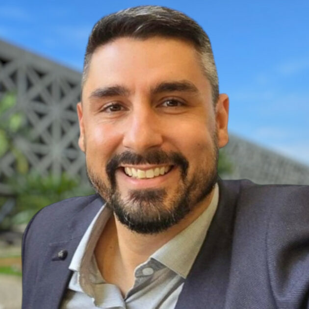 Julio Signorini, Diretor de Cibersegurança da Secretaria de Gestão e Governo Digital do Estado de São Paulo, sorrindo em um ambiente ao ar livre, com fundo de edifício moderno e céu azul