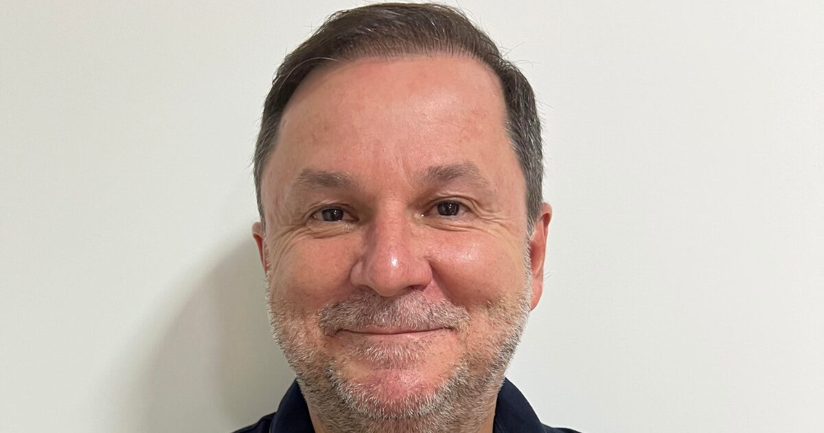 Retrato de Wilian, CIO da Tempo, posando em frente a uma parede branca. Ele está usando uma camisa polo azul escura e exibe um sorriso discreto, com os braços cruzados.