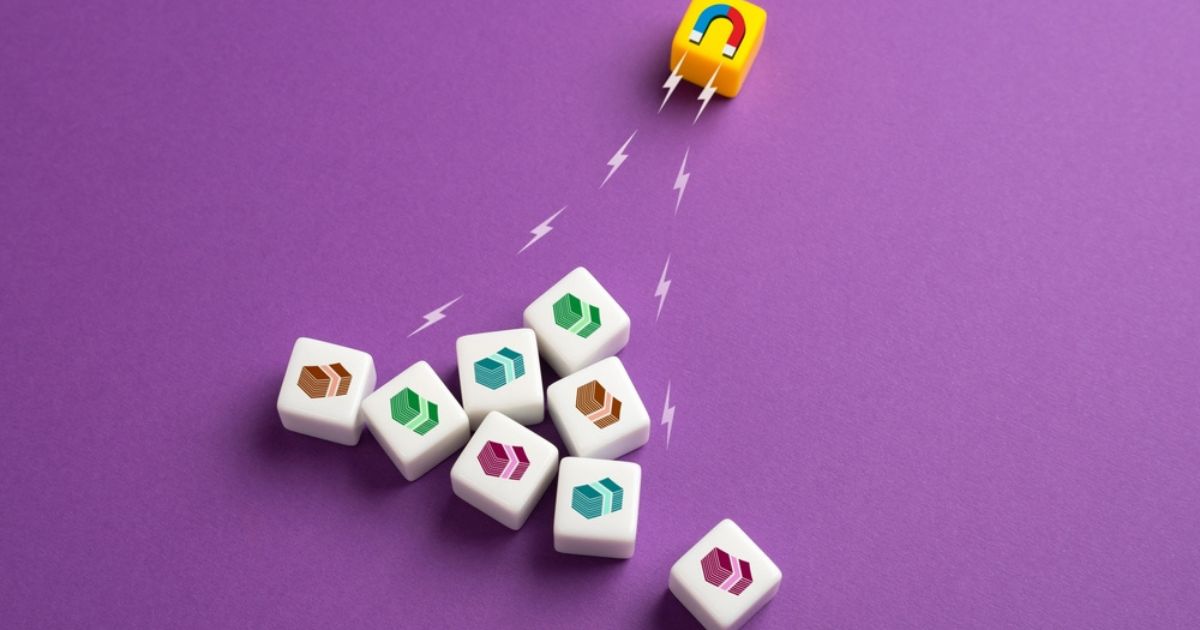 A imagem apresenta um fundo roxo vibrante e contém um conjunto de peças quadradas brancas com ícones coloridos estilizados, organizados de forma irregular. No canto superior direito, um pequeno cubo amarelo com um desenho de um ímã em vermelho e azul parece atrair essas peças, simbolizado por linhas pontilhadas ou raios que representam magnetismo. A composição transmite a ideia de atração, organização ou impacto de forças invisíveis em elementos variados.
