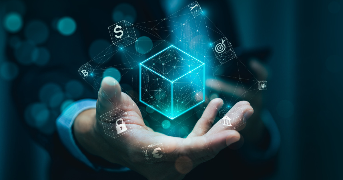 Imagem conceitual de tokenização, mostrando uma mão segurando um cubo digital brilhante no centro, representando tecnologia blockchain. Em torno do cubo, ícones relacionados a finanças, segurança e metas, como cadeado, cifrões e gráficos, conectados por linhas que simbolizam interconexão digital