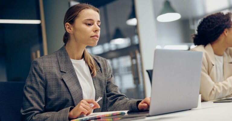 Mulher jovem utilizando um laptop em um ambiente corporativo, representando a prática de literacia ou letramento digital no local de trabalho