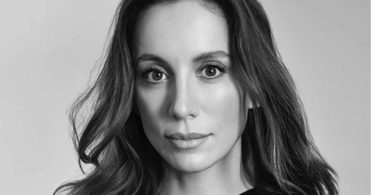 A imagem é um retrato em preto e branco de Mira Murati, ex-CTO da OpenAI. Ela aparece de frente para a câmera, com uma expressão serena e olhar direto. Seus cabelos longos e ondulados emolduram seu rosto, e sua pele tem uma textura suave, realçada pela iluminação equilibrada. O fundo é simples e neutro, destacando ainda mais seus traços faciais