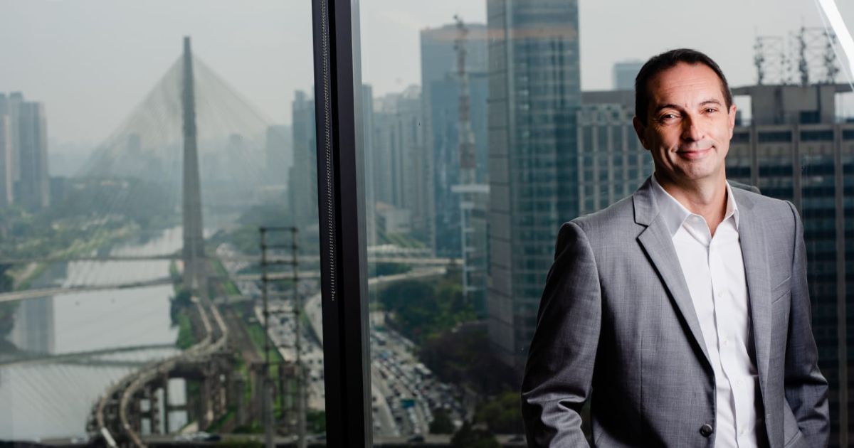 Marcelo Tangione, presidente da Mastercard Brasil, posa em um escritório com vista panorâmica para a cidade de São Paulo, destacando ao fundo a Ponte Estaiada e os arranha-céus da região.