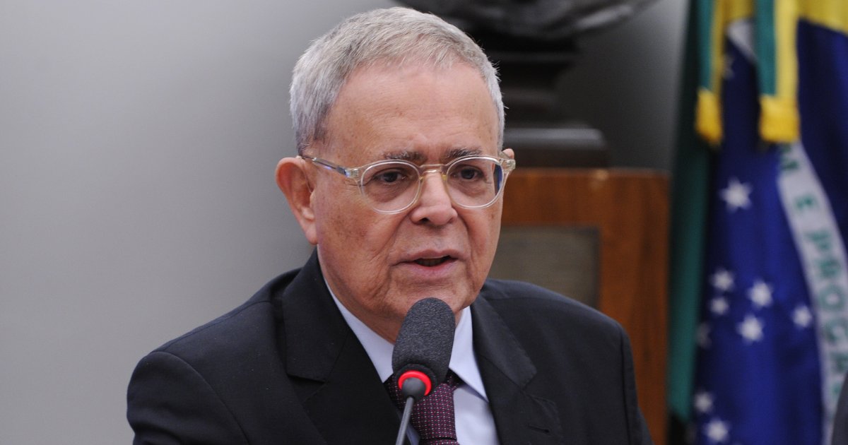 Paulo Milliet Roque, presidente da Abes, em um evento oficial. Ele aparece falando ao microfone, vestindo um terno preto, camisa branca e gravata escura. Usa óculos de armação clara e tem cabelos grisalhos curtos. Ao fundo, há uma bandeira do Brasil e um ambiente formal, sugerindo um contexto institucional ou governamental (Paulo Milliet Roque, Abes, foto agência câmara)