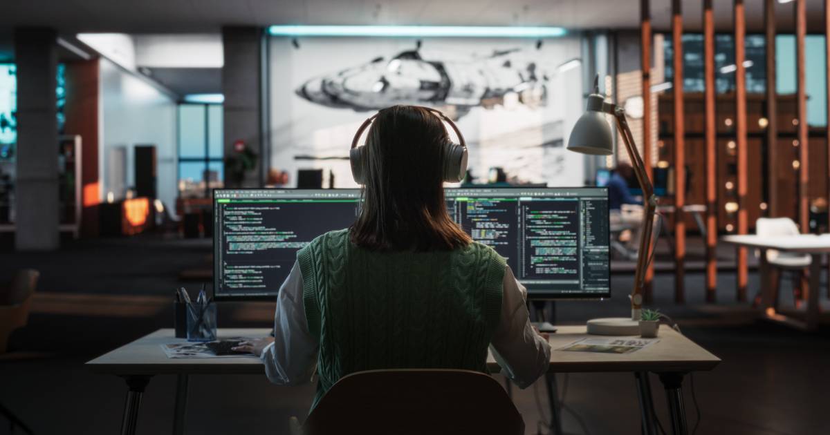 Imagem representando mulheres na tecnologia. Uma programadora, vista de costas, trabalha em frente a dois monitores com códigos de programação. Ela usa fones de ouvido e um colete verde sobre uma blusa branca, em um ambiente moderno e bem iluminado, com elementos de design e um mural futurista ao fundo. A cena destaca a presença feminina na área de tecnologia e inovação, cibersegurança