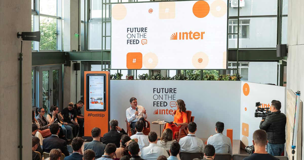 Palestra com público presencial no evento Future on the Feed, promovido pelo Inter. Dois palestrantes sentados no palco, rodeados por público atento e equipamento de filmagem, num espaço moderno com paredes de vidro.