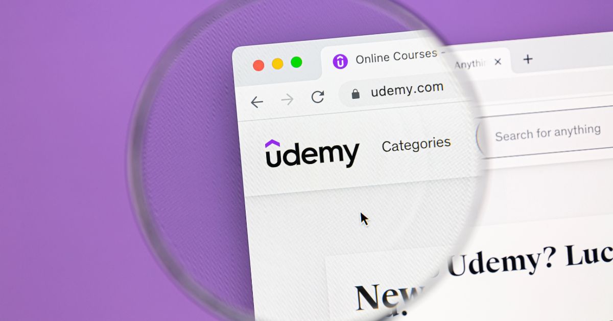 Imagem do site da Udemy ampliada por uma lupa sobre fundo roxo, destacando o logótipo e barra de navegação com a opção de categorias.