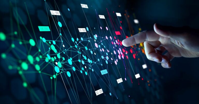 Imagem digital mostrando uma mão humana interagindo com uma interface virtual composta por uma rede de pontos e linhas coloridas conectadas, representando dados ou algoritmos. A interface exibe etiquetas com códigos alfanuméricos e elementos visuais que remetem a conceitos de inteligência artificial, big data ou aprendizado de máquina. O fundo é escuro, destacando os elementos gráficos em tons vibrantes como verde, azul, roxo e vermelho