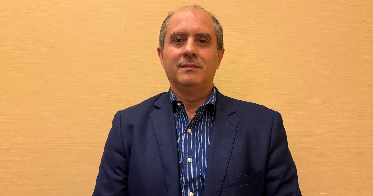 Victor Murad Filho, subsecretário de Transformação do Governo do Espírito Santo, posa em frente a uma parede bege, vestindo blazer azul-marinho e camisa listrada. Foto: Déborah Oliveira.