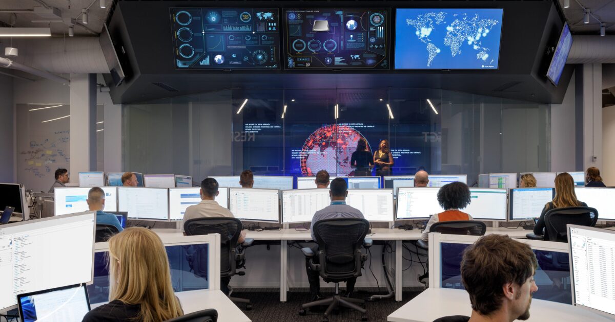 Imagem de um centro de comando de cibersegurança com profissionais monitorando sistemas digitais (setor de segurança)