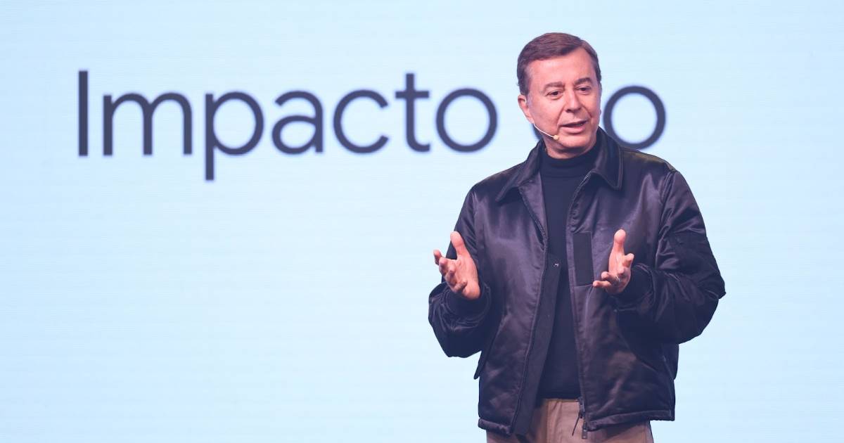 Fábio Coelho, Presidente do Google Brasil, aparece em pé sobre um palco, usando um microfone de cabeça e gesticulando com as mãos enquanto fala. Ele veste uma jaqueta preta e uma camisa preta de gola alta. Ao fundo, vê-se parcialmente a palavra "Impacto" projetada em uma tela branca. A imagem transmite um momento de apresentação ou palestra.