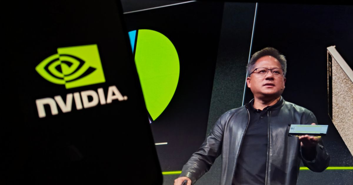 Pessoa com o rosto desfocado segura um dispositivo, possivelmente uma placa gráfica, durante uma apresentação. Ela veste uma jaqueta de couro preta e está posicionada diante de uma tela que exibe o logotipo da NVIDIA e outros elementos gráficos, sugerindo um evento ou anúncio relacionado à tecnologia.