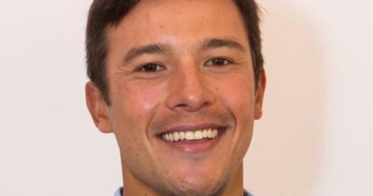 Close-up do rosto de uma pessoa sorridente, olhando diretamente para a câmera. O fundo é neutro, destacando os traços faciais da pessoa. (TotalPass)