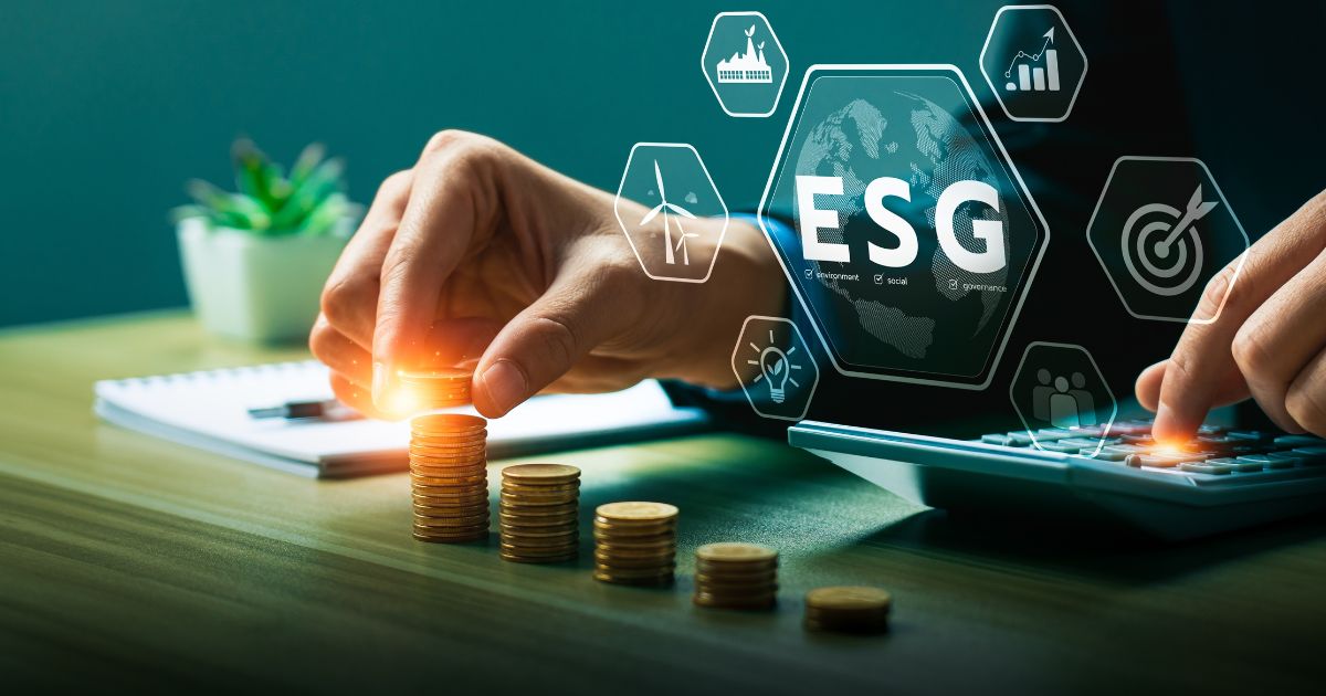 A imagem apresenta um cenário corporativo com foco em finanças e sustentabilidade. No primeiro plano, há uma mão empilhando moedas douradas, formando colunas que sugerem crescimento financeiro. Ao lado, outra mão utiliza uma calculadora, indicando análise ou planejamento econômico. Sobreposto à imagem, há um elemento gráfico com a sigla “ESG” (Environmental, Social, Governance) destacada no centro, acompanhada de ícones relacionados a práticas sustentáveis, responsabilidade social e governança corporativa. Ao fundo, é possível ver um bloco de anotações e uma planta decorativa, reforçando a ideia de equilíbrio entre negócios e meio ambiente. (climáticas)