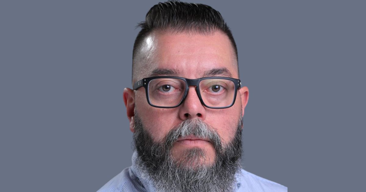 Pessoa vestindo camisa social clara, posicionada de frente para a câmera contra um fundo uniforme em tom cinza. O enquadramento é centralizado e destaca a parte superior do tronco, incluindo a gola da camisa e parte da barba, transmitindo um contexto profissional e neutro. (Luiz Eduardo, CTO Global de Segurança da HPE Networking)