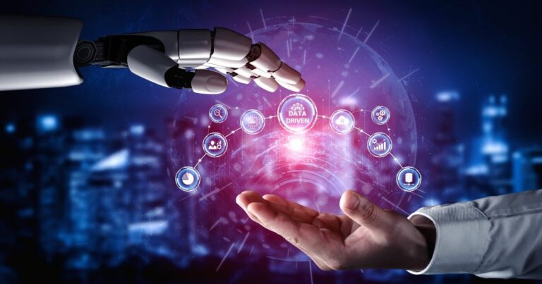 Mão robótica estendida em direção a uma mão humana, ambas posicionadas frente a frente. Entre elas, aparece uma interface digital holográfica com ícones interligados e o texto “Data Driven”, simbolizando integração entre inteligência artificial, análise de dados e tomada de decisões tecnológicas em um ambiente futurista. (inteligência analítica)