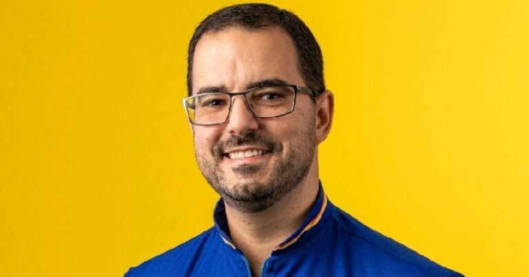 Pessoa vestindo uma camisa azul vibrante com detalhes amarelos na gola, posicionada diante de um fundo amarelo sólido que cria um contraste marcante e visualmente chamativo. (Ipiranga)