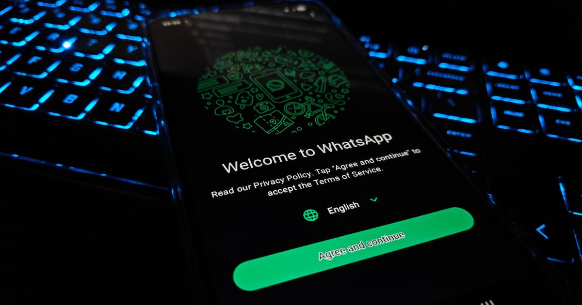 Tela de um smartphone exibindo a página inicial do WhatsApp com a mensagem “Welcome to WhatsApp”, posicionada sobre um teclado iluminado por luz azul. O botão verde “Agree and Continue” aparece em destaque na parte inferior da tela, sugerindo o início do processo de configuração do aplicativo. (India)